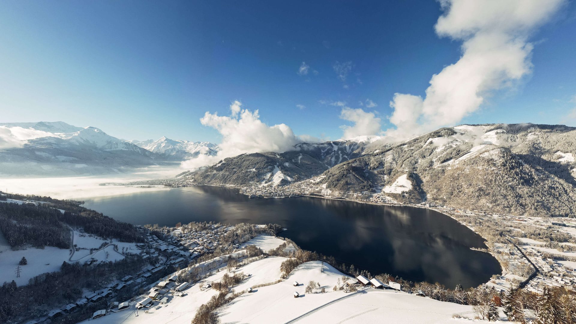 Schneebedeckte Landschaft rund um den Zeller See mit Bergen und blauem Himmel.